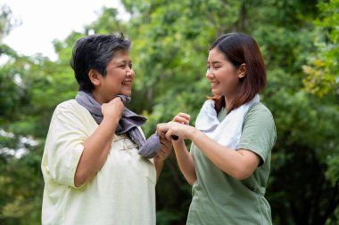 Parkta sabah egzersizinde birlikte çalışan çekici bir anne ve kız çocuğu. Kız, annesinin terini beyaz havluyla, yaşlı bir bakıcı ve mutlu bir aile kavramı ile emiyor..