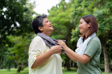 Parkta sabah egzersizinde birlikte çalışan çekici bir anne ve kız çocuğu. Kız, annesinin terini beyaz havluyla, yaşlı bir bakıcı ve mutlu bir aile kavramı ile emiyor..