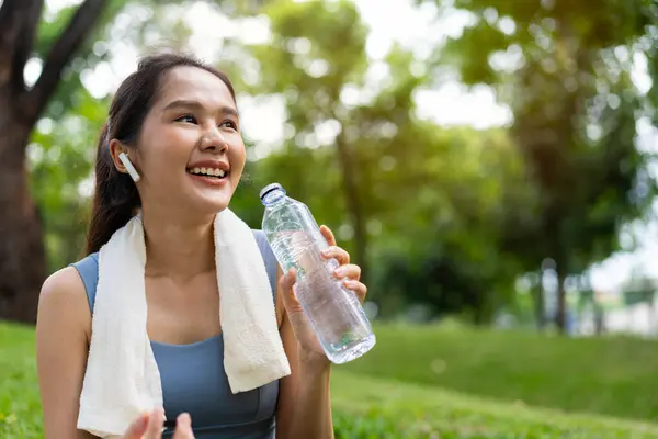 Asian young women drink water from a plastic bottle after exercises or sports. Asian woman running in garden. Beautiful fitness athlete woman drinking pure water after workout exercise on morning