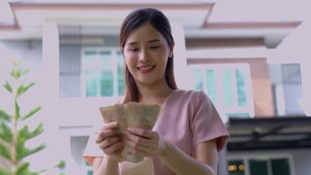 家の前に多くの紙幣を持っている幸せな魅力的なアジアの女性の肖像画を祝い 家の最終的なインストールを支払うために 不動産コンセプトのための融資 若い笑顔 — ストック動画
