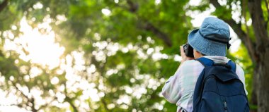 Sırtında kamera ve sırt çantası tutan Asyalı olgun bir kadının portresi. Asya 'da etkin bir son sınıf öğrencisi parkta doğanın tadını çıkarıyor. Açık havada bir ormanda bir patikada dikiliyorum. Aktif seyahatin tadını çıkarıyorum.