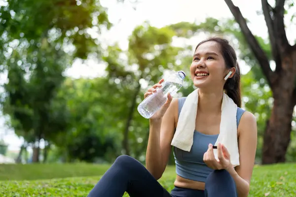 Asian young women drink water from a plastic bottle after exercises or sports. Asian woman running in garden. Beautiful fitness athlete woman drinking pure water after workout exercise on morning