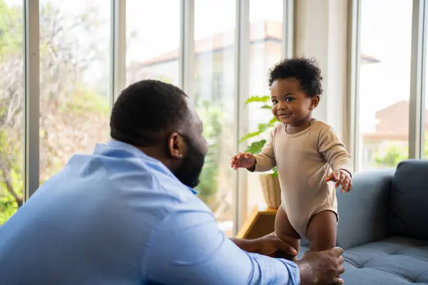 Portrait Of Happy African American Dad With Cute Little Baby Girl on couch at home in the living room, caring father smiling and amusing his girl while sitting on the couch, happy family