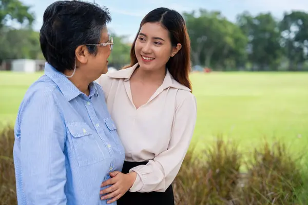 Portrait of Asian mother and Grown daughter showing love and hug and happy moment. Happy Mother Day, Asian careful caregiver or nurse hold the patient hand and encourage the patient in a garden