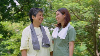 Parkta sabah egzersizinde birlikte çalışan çekici bir anne ve kız çocuğu. Kız, annesinin terini beyaz havluyla, yaşlı bir bakıcı ve mutlu bir aile kavramı ile emiyor..