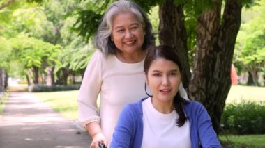 Parkta tekerlekli sandalyedeki mutlu genç kadın annesiyle birlikte, tekerlekli sandalyedeki muhteşem kız yeni güne seviniyor, pozitif duygu ve duygu. Neşe, fiziksel iyileşme kavramı