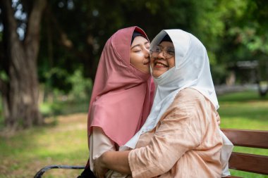 Muslim careful caregiver or nurse taking care of the patient in the hospital park. Happy Muslim mother in hijab hugging daughter. Concept of Savings and Senior Health Insurance, a Happy Family clipart