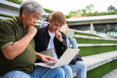 Üniversitede Capstone projesi için yaşlı öğretmenleri dinleyen odaklanmış genç öğrenciler. Mezuniyet projesi için öğrencilerle birlikte çalışan orta yaşlı mutlu öğretmen..