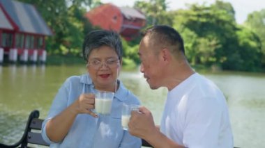 Bir adam ve bir kadın gölün kenarındaki bankta oturuyorlar. Adam bir fincan süt tutuyor ve kadın bir fincan kahve tutuyor. İkisi de gülümsüyor ve birbirlerine eşlik etmekten zevk alıyor gibi görünüyorlar.