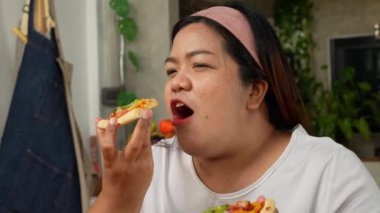 Pişmiş pizzadan sonra evde ev yapımı pizza yiyen mutlu Asyalı kadın. Şişman kadınlar yemekten hoşlanır. Aşırı yeme bozukluğu, abur cubur ve sağlıksız gıdalar yeme düşüncesi..