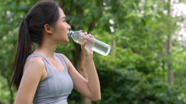 Genç Asyalı kadınlar spor ve egzersizden sonra plastik şişeden su içerler. Bahçede koşan Asyalı kadın. Güzel fitness atleti kadın sabah egzersizinden sonra saf su içiyor.