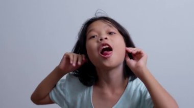 Küçük komik Asyalı kız kameraya bakıp yanaklarını işaret eden, çocukluk tanıklığı konseptinin tadını çıkaran, pozitif çocuk, 4k görüntü, Yavaş Hareket Portresi