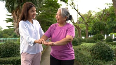 Yaşlı bir Asyalı kadın yürüteç kullanıyor ve kızıyla bahçede yürüyor. Mutlu emeklilik kavramı. Bakıcının, birikimin, sağlık sigortasının ve sağlık hizmetlerinin bakımıyla.