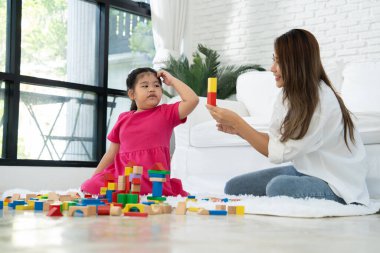 Kiraz rengi genç anne, Down sendromlu kızıyla renkli oyuncak bloğu oynar. Renkli tahta oyuncaklar, gelişimi arttırmak ve yavaş yavaş öğrenme becerilerini artırabilir.