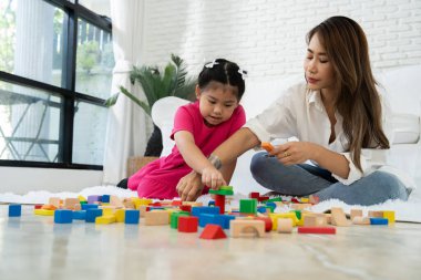 Kiraz rengi genç anne, Down sendromlu kızıyla renkli oyuncak bloğu oynar. Renkli tahta oyuncaklar, gelişimi arttırmak ve yavaş yavaş öğrenme becerilerini artırabilir.
