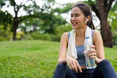 Genç Asyalı kadınlar spor ve egzersizden sonra plastik şişeden su içerler. Bahçede koşan Asyalı kadın. Güzel fitness atleti kadın sabah egzersizinden sonra saf su içiyor.