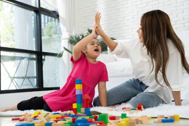 Kiraz rengi genç anne, Down sendromlu kızıyla renkli oyuncak bloğu oynar. Renkli tahta oyuncaklar, gelişimi arttırmak ve yavaş yavaş öğrenme becerilerini artırabilir.