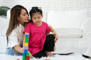 Kiraz rengi genç anne, Down sendromlu kızıyla renkli oyuncak bloğu oynar. Renkli tahta oyuncaklar, gelişimi arttırmak ve yavaş yavaş öğrenme becerilerini artırabilir.