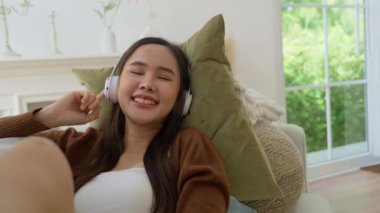 Evde bir kanepede dinlenen ve internetten müzik dinleyen, kulaklıklı genç Asyalı kadın. Düz dinlenme, oturma odasında boş zaman geçir. Salon konsepti