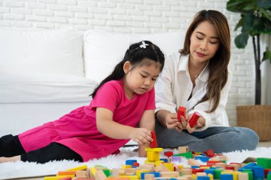 Kiraz rengi genç anne, Down sendromlu kızıyla renkli oyuncak bloğu oynar. Renkli tahta oyuncaklar, gelişimi arttırmak ve yavaş yavaş öğrenme becerilerini artırabilir.