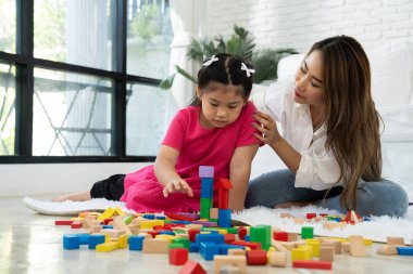 Kiraz rengi genç anne, Down sendromlu kızıyla renkli oyuncak bloğu oynar. Renkli tahta oyuncaklar, gelişimi arttırmak ve yavaş yavaş öğrenme becerilerini artırabilir.