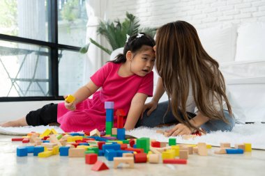 Kiraz rengi genç anne, Down sendromlu kızıyla renkli oyuncak bloğu oynar. Renkli tahta oyuncaklar, gelişimi arttırmak ve yavaş yavaş öğrenme becerilerini artırabilir.