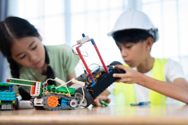 İş yerinde genç bir mühendis: Güvenlik kaskı takan odaklanmış genç bir çocuk, renkli yapı taşlarından titizlikle bir robot monte ediyor, STEM eğitim ve mühendislik tutkusunu gözler önüne seriyor.