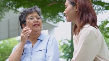 Asyalı genç torunun parkta yaşlı bir büyükanneyle sohbete girişinin iç açıcı görüntüsü. İkisi de gerçek bir neşe ve açık hava ortamında kahkahalarını paylaşıyor. Nesil Sevgisi