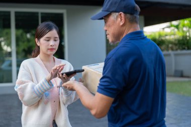 Neşeli Asyalı kadınlar teslimat servisinden ürün kutusu alıyorlar ve akıllı telefondan QR kodunu taratarak, ev teslimatları, uygun bir alışveriş deneyimi ve güvenilir bir kapı servisi konseptiyle ödeme yapıyorlar.