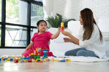 Kiraz rengi genç anne, Down sendromlu kızıyla renkli oyuncak bloğu oynar. Renkli tahta oyuncaklar, gelişimi arttırmak ve yavaş yavaş öğrenme becerilerini artırabilir.
