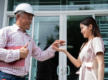 Mutlu Yeni Ev Sahibi: Gülümseyen bir mimar ya da müteahhit yeni evinin önünde mutlu bir genç kadına anahtarları verir.