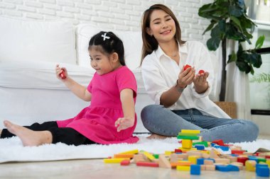 Kiraz rengi genç anne, Down sendromlu kızıyla renkli oyuncak bloğu oynar. Renkli tahta oyuncaklar, gelişimi arttırmak ve yavaş yavaş öğrenme becerilerini artırabilir.