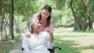 Tekerlekli sandalyedeki hastayla ilgilenen Asyalı dikkatli bir bakıcı ya da hemşire. Bakıcının, birikimin ve sağlık sigortasının özenle mutlu emeklilik kavramı. Mutlu bir aile.