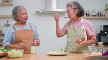 İki yaşlı kadın dostça bir yemek hazırlıyor, taze malzemelerle lezzetli bir yemek hazırlıyor ve birbirlerinin keyfini çıkarıyorlar, evlerinde keyifli bir aşçılık deneyimi yaşıyorlar.