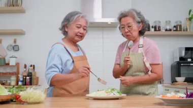 İki yaşlı kadın dostça bir yemek hazırlıyor, taze malzemelerle lezzetli bir yemek hazırlıyor ve birbirlerinin keyfini çıkarıyorlar, evlerinde keyifli bir aşçılık deneyimi yaşıyorlar.