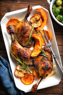 Elma, portakal ve kabak dilimleriyle kızartılmış ördek bacakları kırsal ahşap masada.