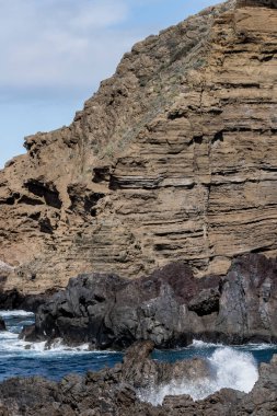 Portekiz 'in Porto Moniz şehrinde parlak sonbahar ışığında çekilen bazalt ve trachyte volkanik kayalıkları ile Madeira adasındaki okyanus manzarası.