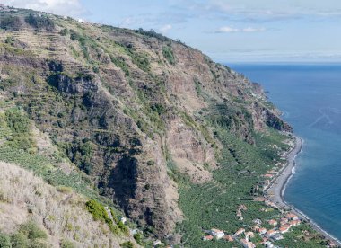 Portekiz, Ponta do Sol 'da parlak sonbahar ışığı altında Madeira Adası' nın güney Atlantik kıyısında dik yamaçlar altında muz yetiştirilen hava manzarası.