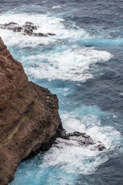 Portekiz, Ponta da Rosto 'da parlak bir sonbahar ışığı altında çekilen Madeira adasındaki volkanik kayalıklara çarpan okyanus dalgalarıyla dolu manzara.