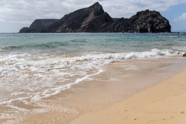 Cal Adası ve Portekiz 'in Porto Santo adasında parlak sonbahar ışığı altında çekilen Calheta sahilindeki altın çubuklu kumların üzerindeki okyanus dalgaları.