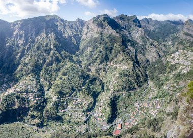 Portekiz 'in başkenti Miradouro Eira do Serrado' dan parlak bir sonbahar ışığı ile çekilen Madeira adasının iç kısımlarındaki Curral des Freires 'in dik volkanik yamaçları ve dağ köyleri.