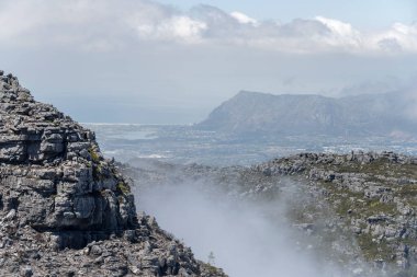 Muizenberg dağları arka planda, Cape Town, Batı Cape, Güney Afrika 'da, parlak yaz ışığında dağın tepesinden çekilen, Masa Dağı' nda alçak bulutlardan kaya uçurumları olan hava manzarası.