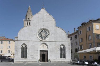 Muggia, Trieste, Friuli, İtalya 'da parlak ışıkta çekilen Santi Giovanni ve Paolo kilisesinin ön cepheleriyle şehir manzarası.