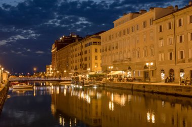 TRIESTE, ITALY - 29 Mayıs 2023: Canal Grande 'de anıtsal cephelerin altında, 29 Mayıs 2023' te Trieste, Friuli, İtalya 'da çekilen gecenin tadını çıkaran insanlarla şehir manzarası