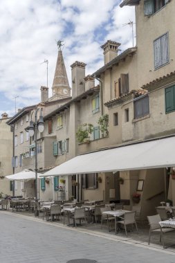  Grado, Gorizia, Friuli, İtalya 'daki tarihi şehrin eski binaları arasında tentente altında boş restoran masalarıyla dolu şehir manzarası