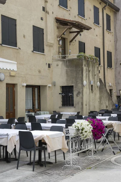 stock image  cityscape with empty restaurant tables in street among old buildings of historical town, shot in bright light at Grado, Gorizia, Friuli, Italy