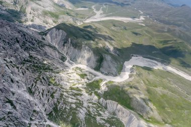 Prena 'nın çorak yamaçlarında, Calascio, Apennines, L' Aquila, Abruzzo, İtalya yakınlarındaki parlak yaz ışığında güneydoğudan çekilen, Laga dağ sırasının çorak yamaçlarında geniş bir vadi bulunan bir planör uçağından gelen hava manzarası.