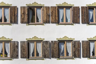 Almanya 'nın Obertstdorf kentindeki turistik dağ köyünde parlak yaz ışığında çekilen, eski geleneksel evin pencerelerinde süslü panjurlar.