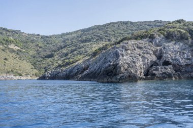 Cacciarella Burnu 'nun batı kayalıklarıyla Akdeniz kıyısında, Arjantario, Tuscany, İtalya' da sonbahar güneşinde parlak bir tekneden çekilen manzara.