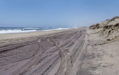 Naukluft Çölü kıyısındaki büyük kumsalda lastik izleri olan manzara, Walvis Körfezi, Namibya, Afrika 'daki parlak bahar ışığı altında çekildi.
